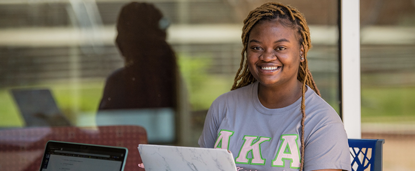 Female student sitting outside at a table working on a laptop.