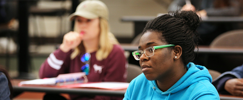 Female student with glasses sitting in classroom listening to lecture,