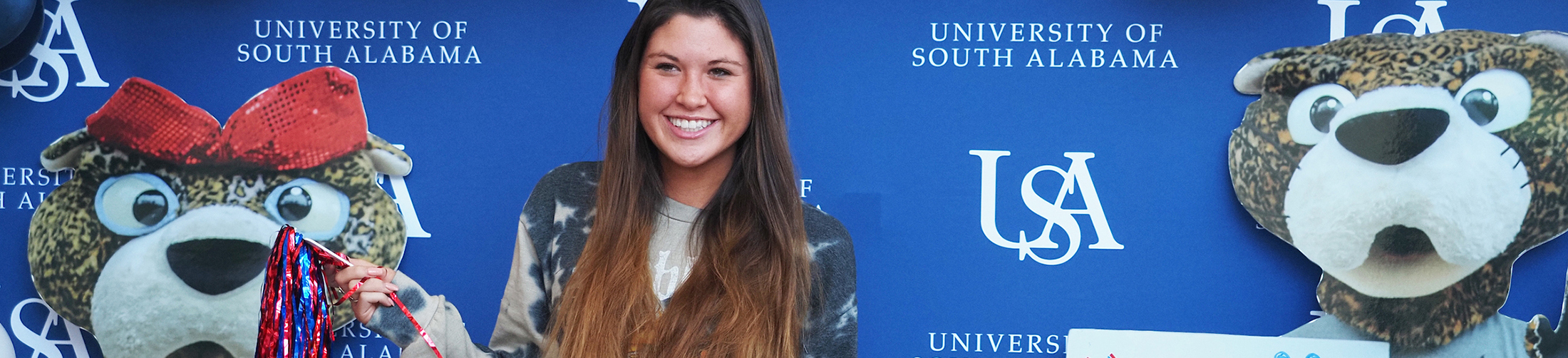 Student smiling in front of South backdrop holding shakers.