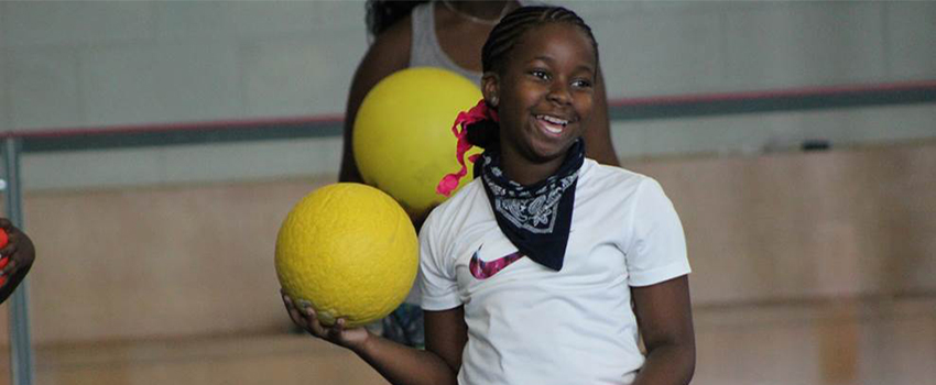 Girl holding ball in gym smiling.