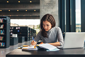 Person writing on notebook at table in library,