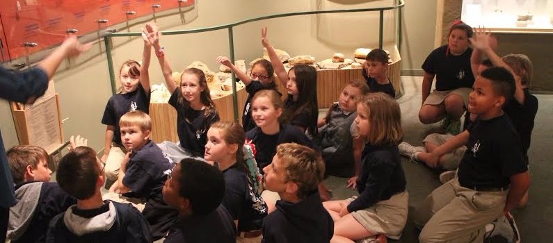 students seated on museum floor listening to leader